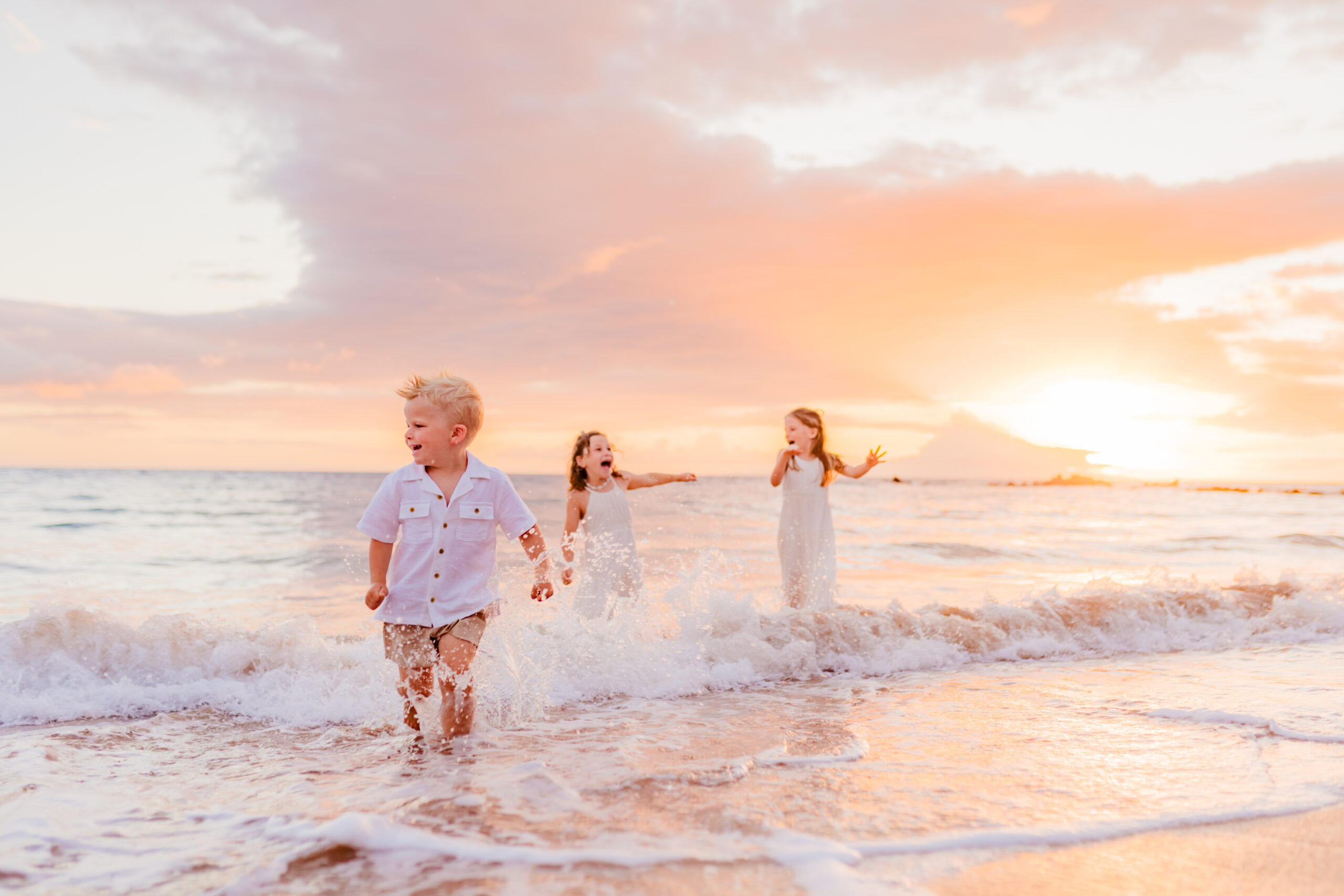 Three siblings play in the ocean together at sunset during their family photoshoot on Maui