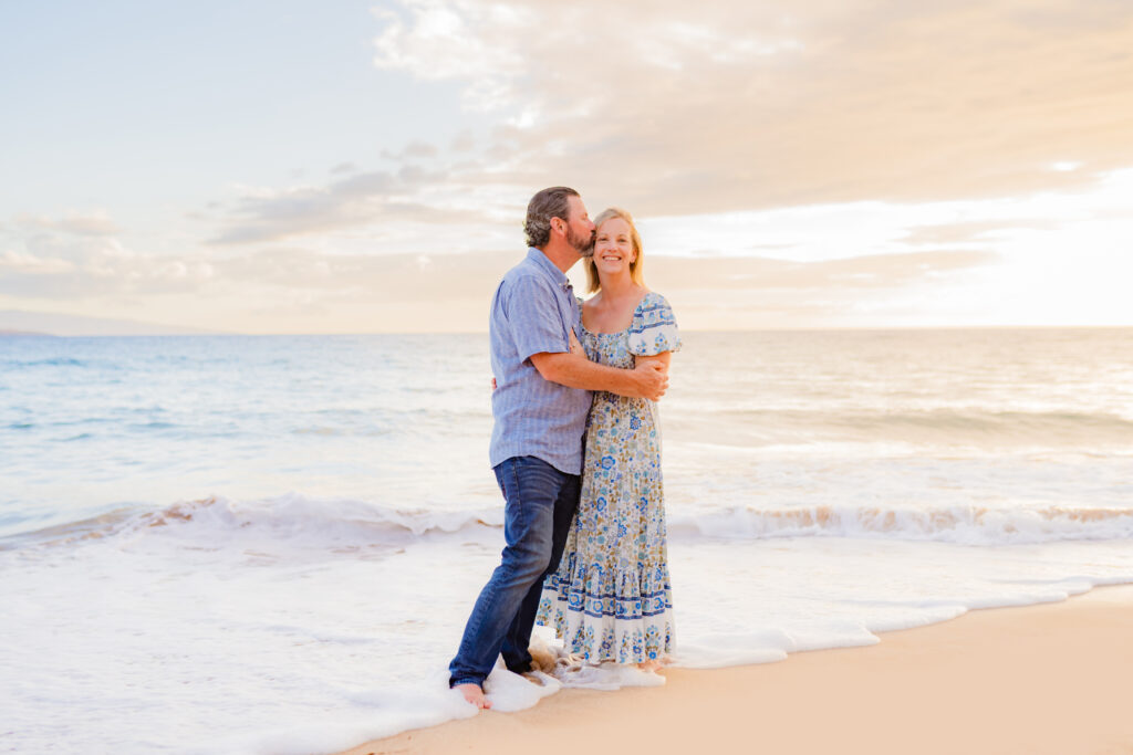 a man leans in and kisses his wife during their sunset beach family photoshoot