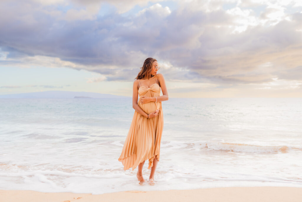 Pregnant woman in flowy beige dress accentuates her bump for her maternity photographer