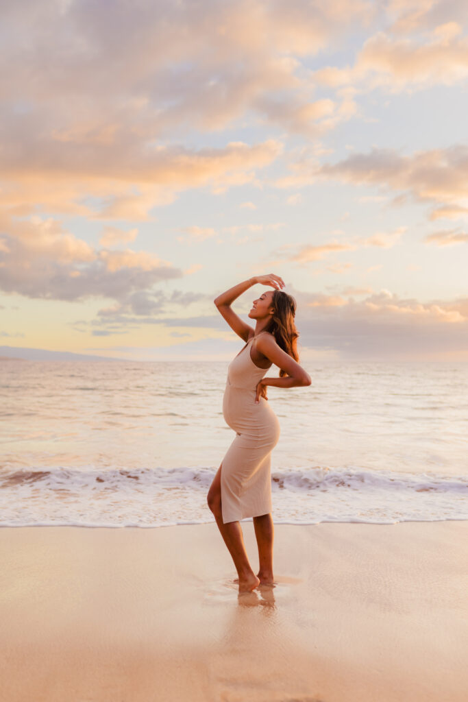 Woman in beige dress shows off her pregnancy bump at the beach