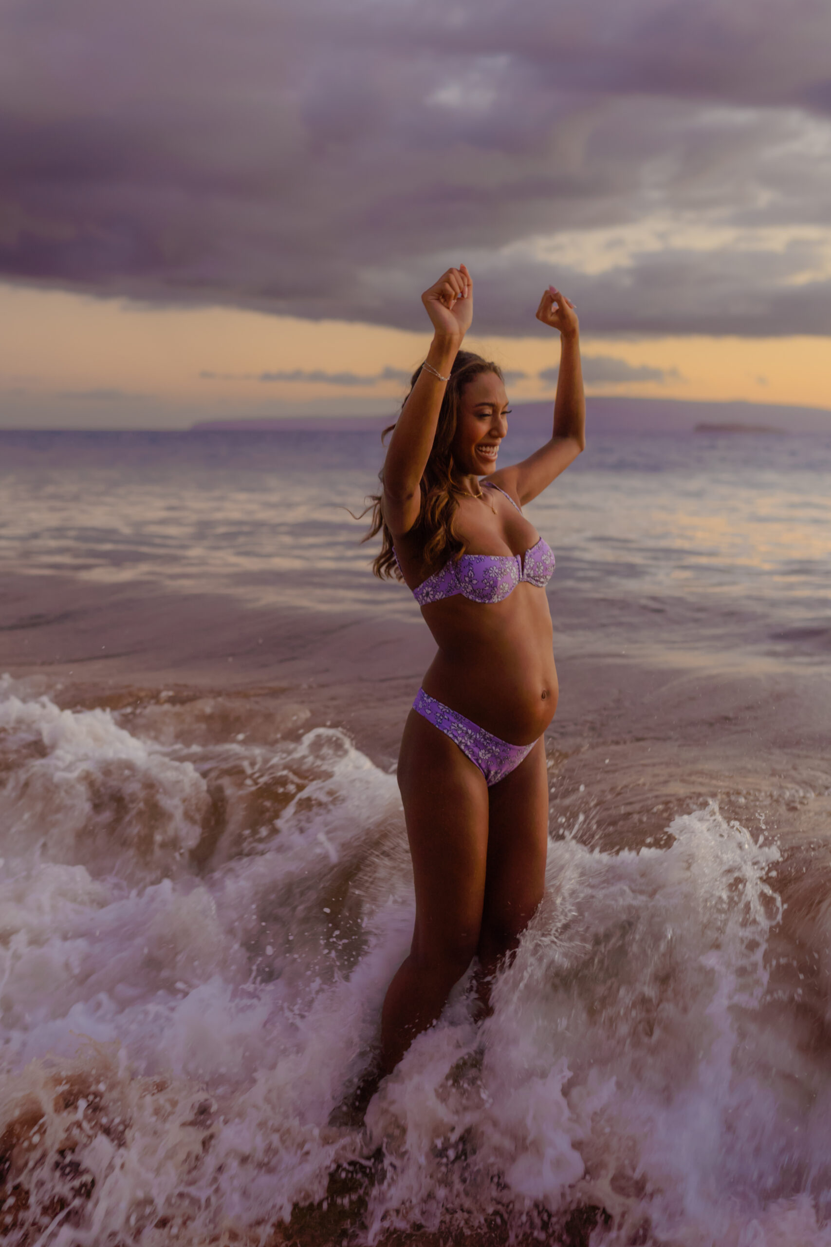 woman splashes in the waves on Maui for her pregnancy photos