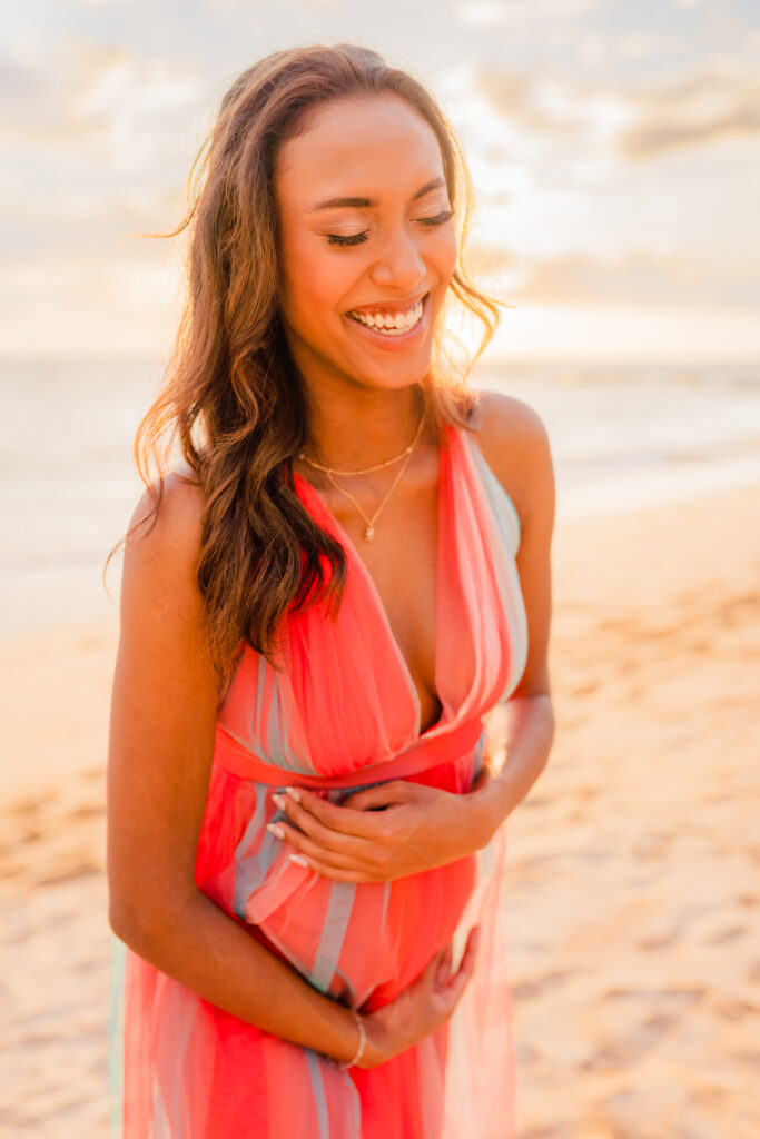 Woman smiles at the beach during sunset on Maui for her babymoon photos