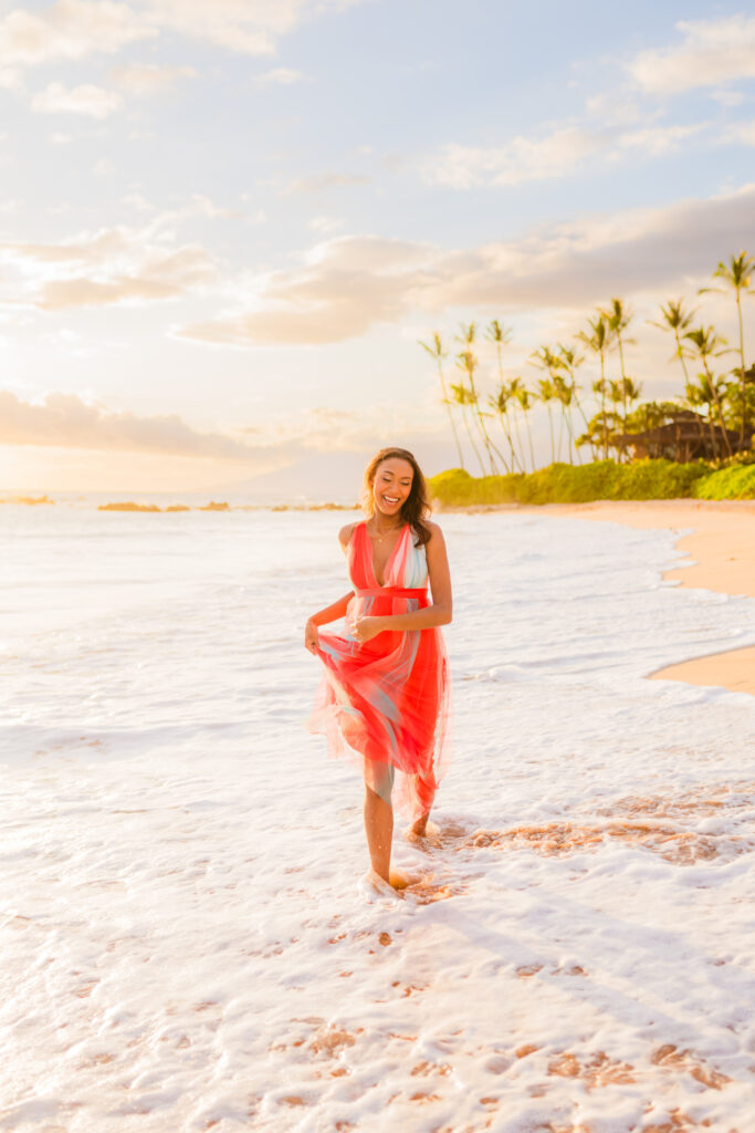 Woman strolls on the beach enjoying the Maui sunset during her babymoon vacation