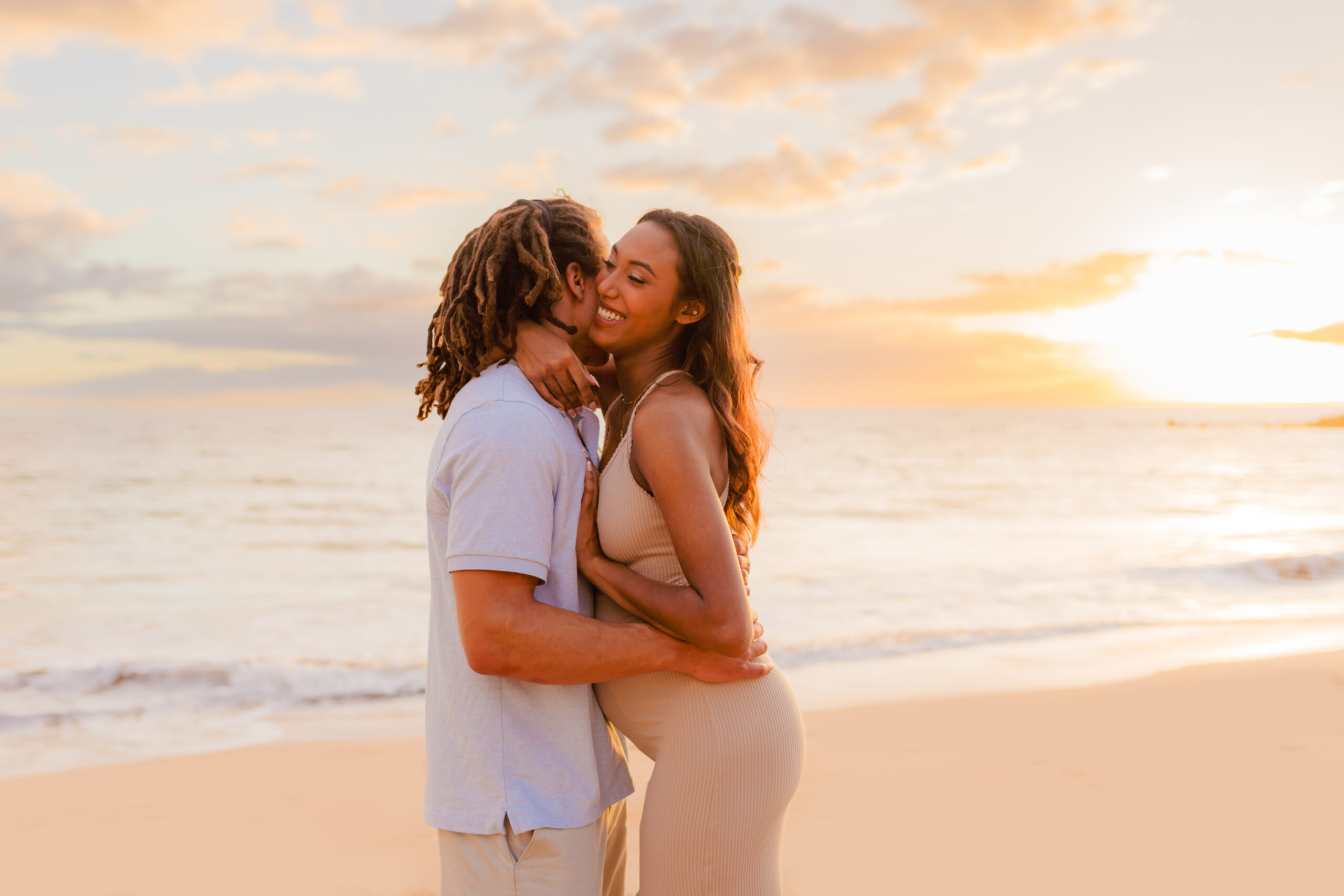 Couple embraces at the beach on their babymoon while their maternity photographer captures the moment