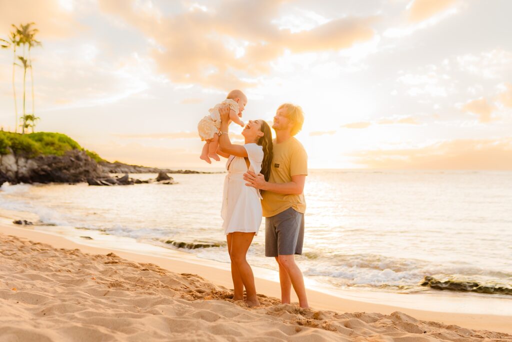 Mom lifts infant and smiles at sunset with family photoshoot by Love and Water Photography Maui