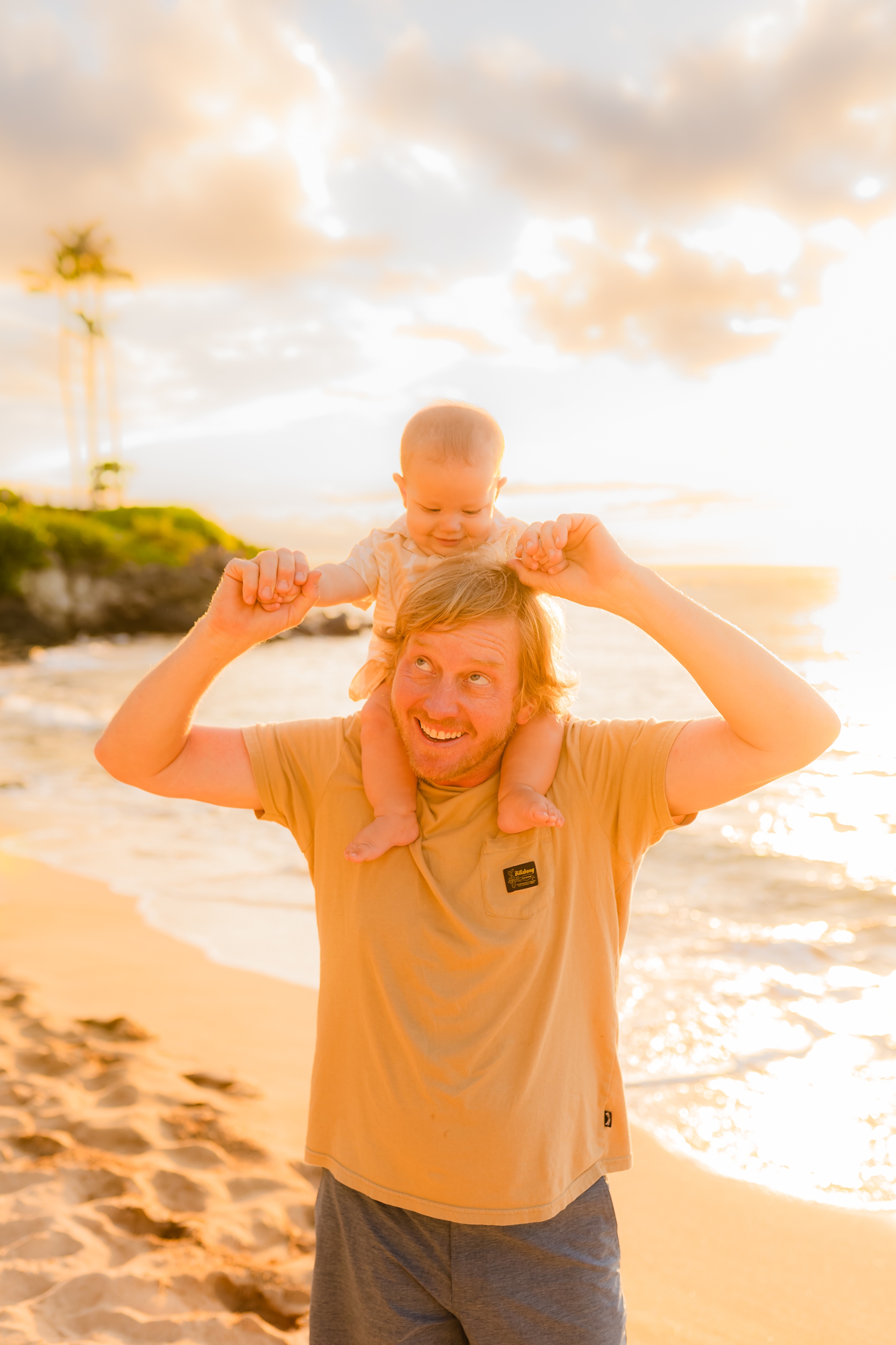 man with baby on shoulders smiling as they enjoy sunset in kapalua bay maui