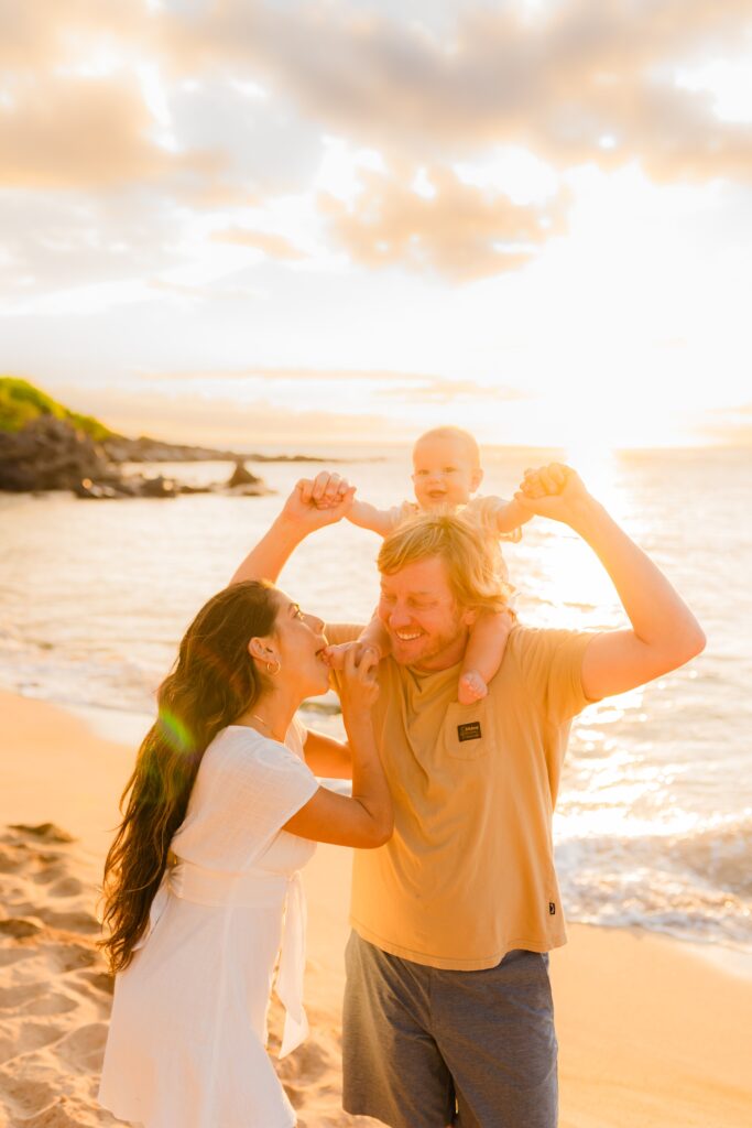 West Maui family photoshoot featuring mom nibbling on young son's toes as he smiles at camera and dad smiles at mom on Maui