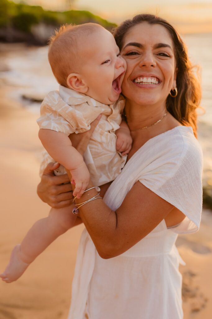 Infant boy in mother's arms laughs and smiles for their Love and Water family photo session in Kapalua