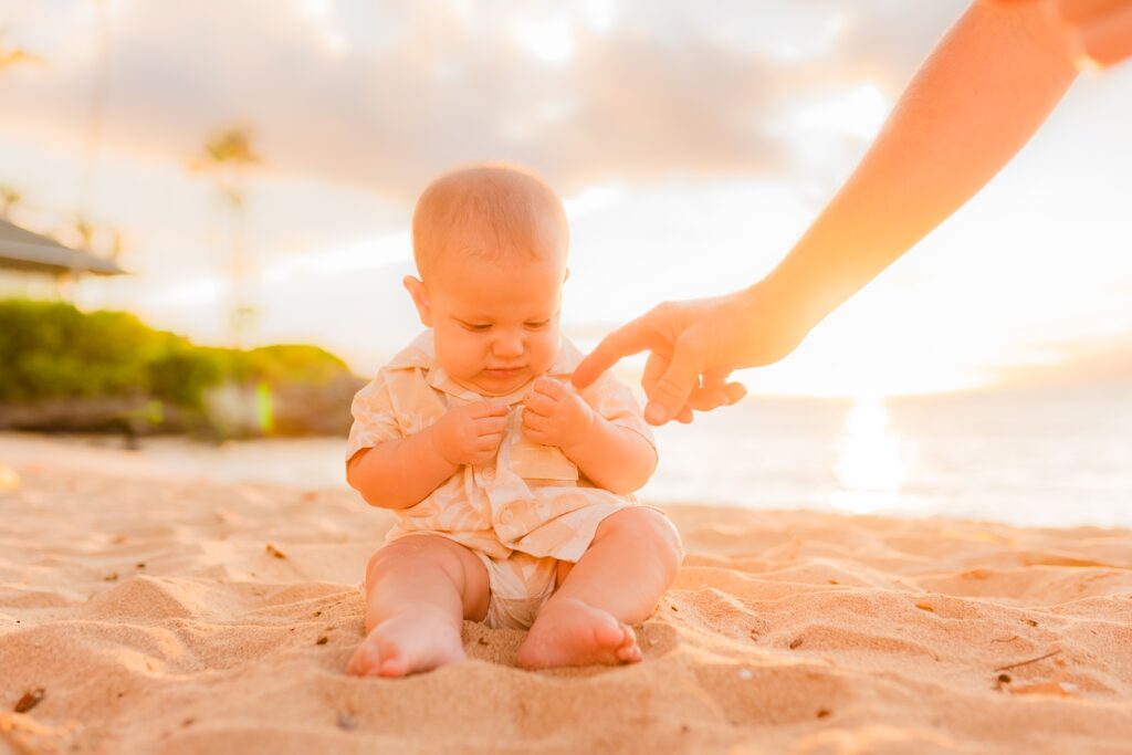 Parent hand pointing at sand held by young son in Maui while sitting on the beach