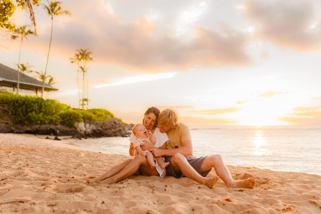 Mom and dad hold their son on the sand at the beach in Kapalua Bay, Maui during Love and Water family photoshoot