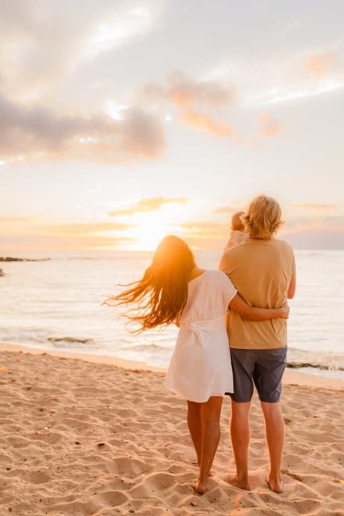 Vertical image of young family of three walking away from the camera toward the sunset at the beach at Kapalua Bay, Maui