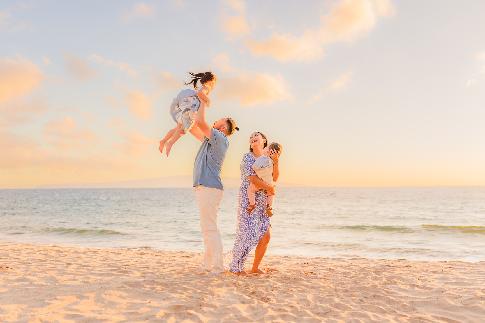 Dad throws daughter in the air as mom holds her son and smiles at the beach in Wailea photographed by Love and Water in Hawaii