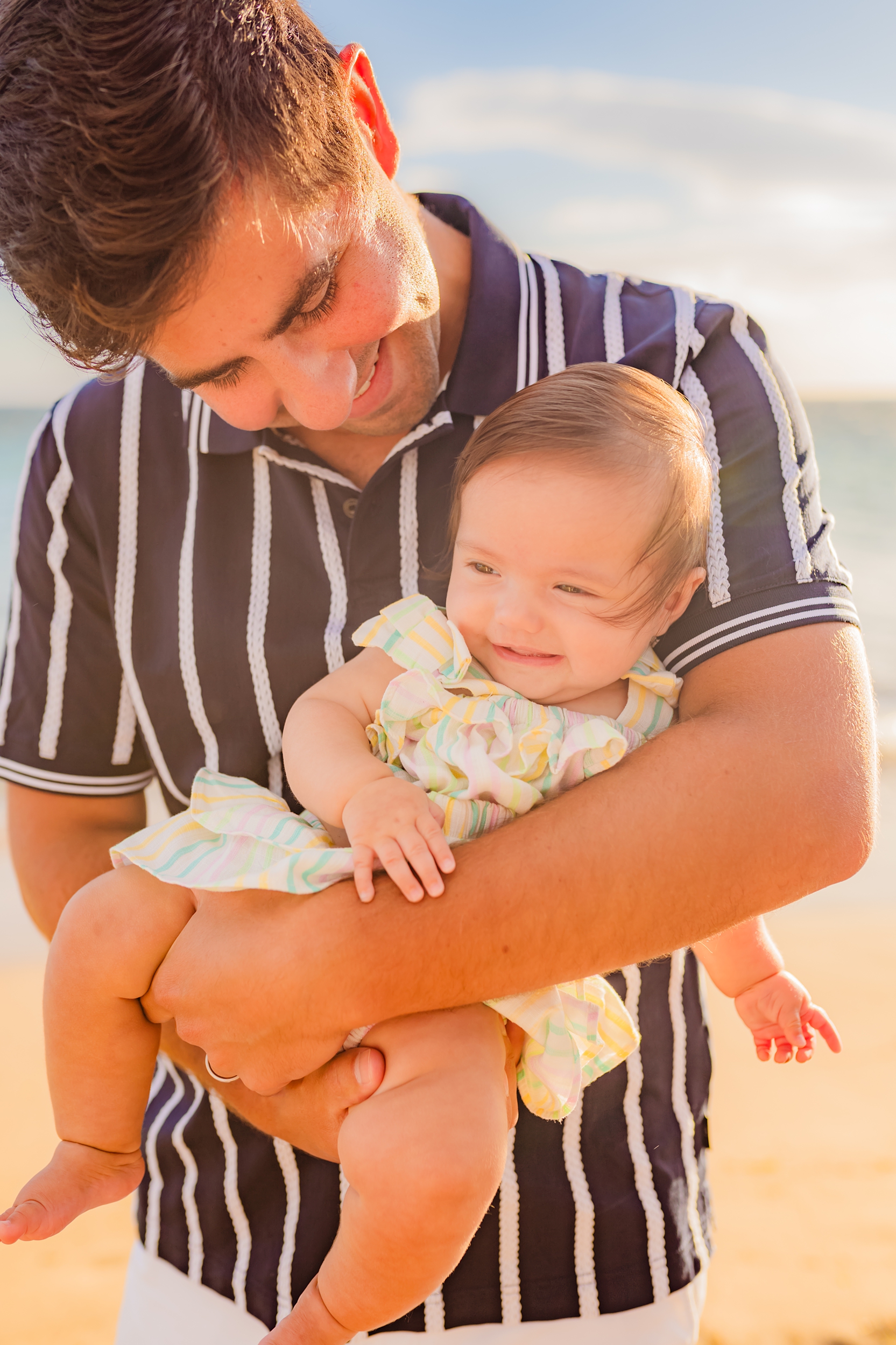 sweet portrait of dad holding newborn daughter on the beach in hawaii during family session at sunset