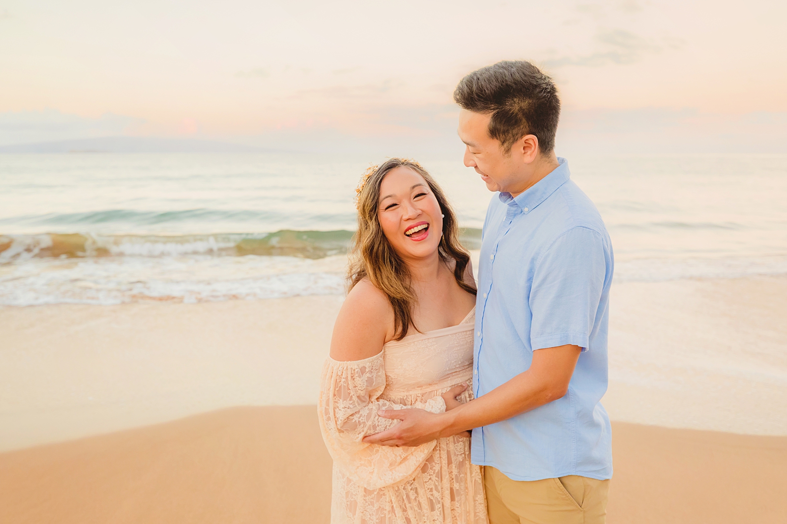 couple laughs and smiles while husband holds his wife's pregnant belly
