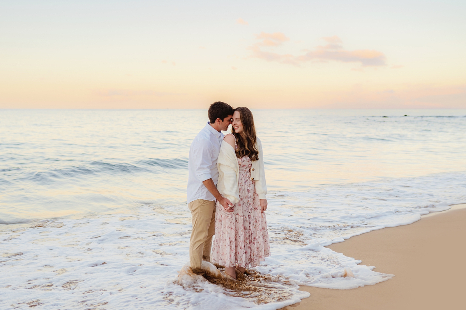couple holding one another at the beach in maui while he kisses her cheek