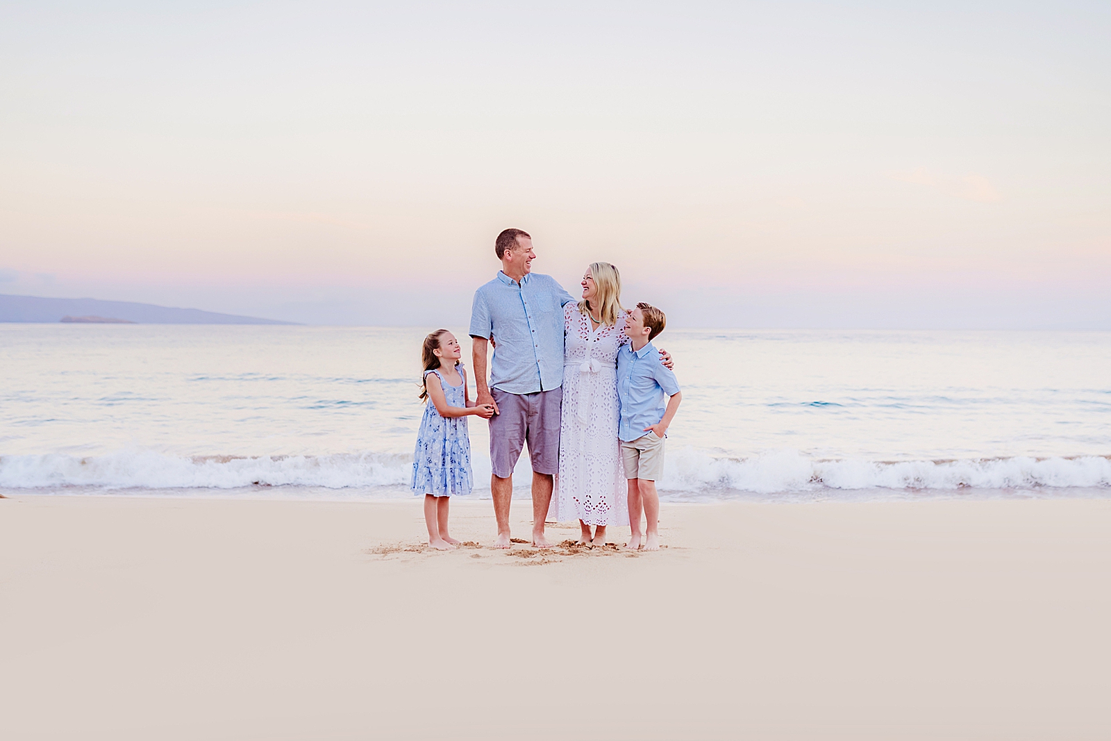 family embracing at sunrise laughing and smiling at one another during portraits at the beach