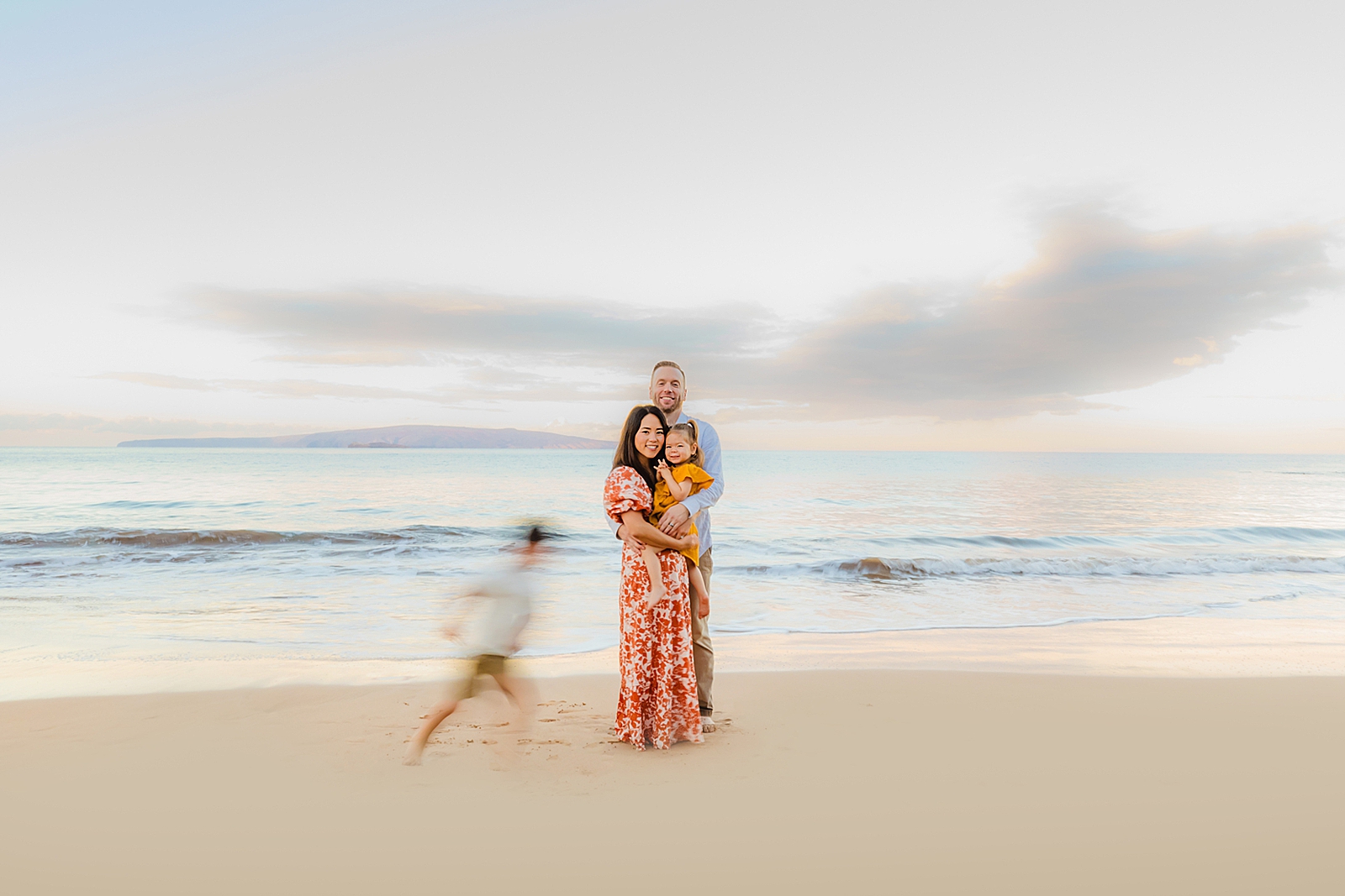 young girl running around mom and dad at the beach during sunrise photoshoot on maui