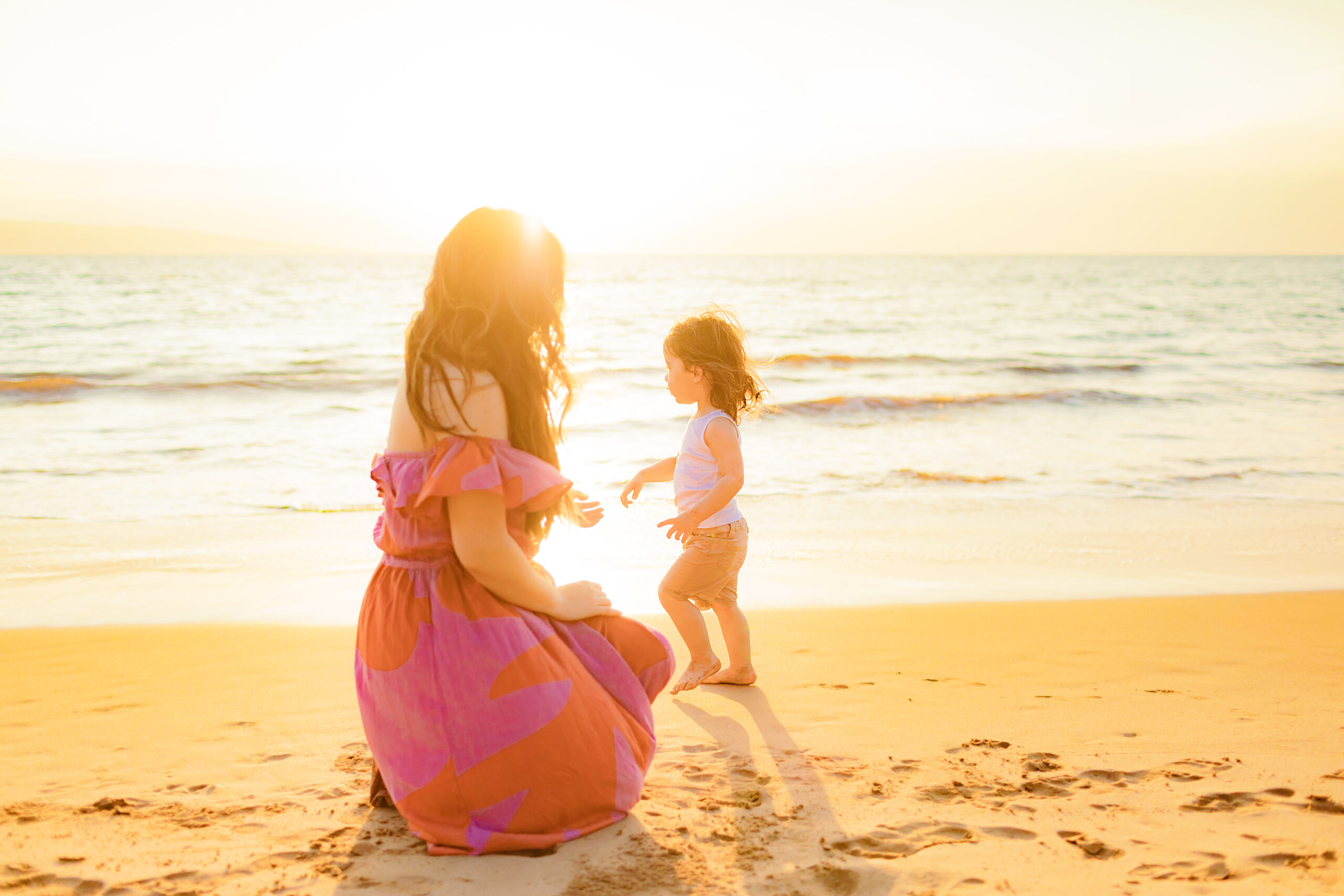 woman in purple and orange dress sits with her child on a beach in Hawaii