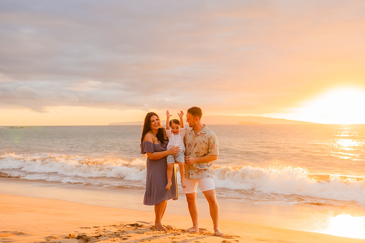 A family of three standing on the beach for family maternity photos in Hawaii at sunset.