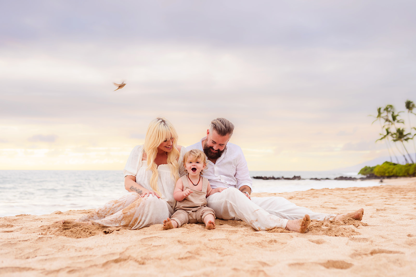 A beautiful family sits on the beach for maternity family photos on Maui with love + water photography.