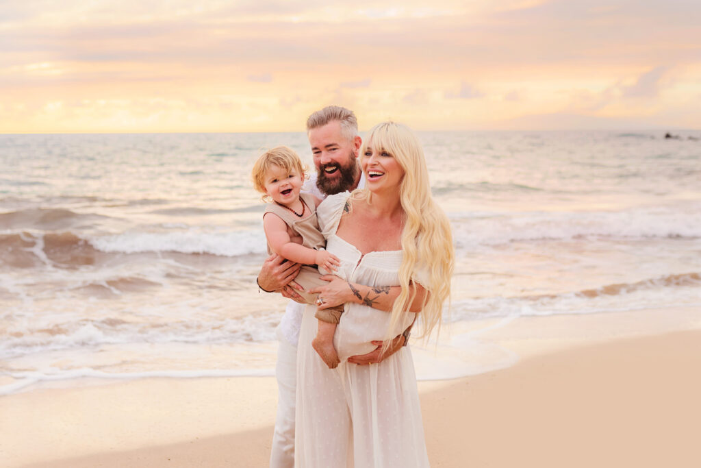 A beautiful family smiling together on the beach for a family maternity photoshoot at sunset with love + water photography.