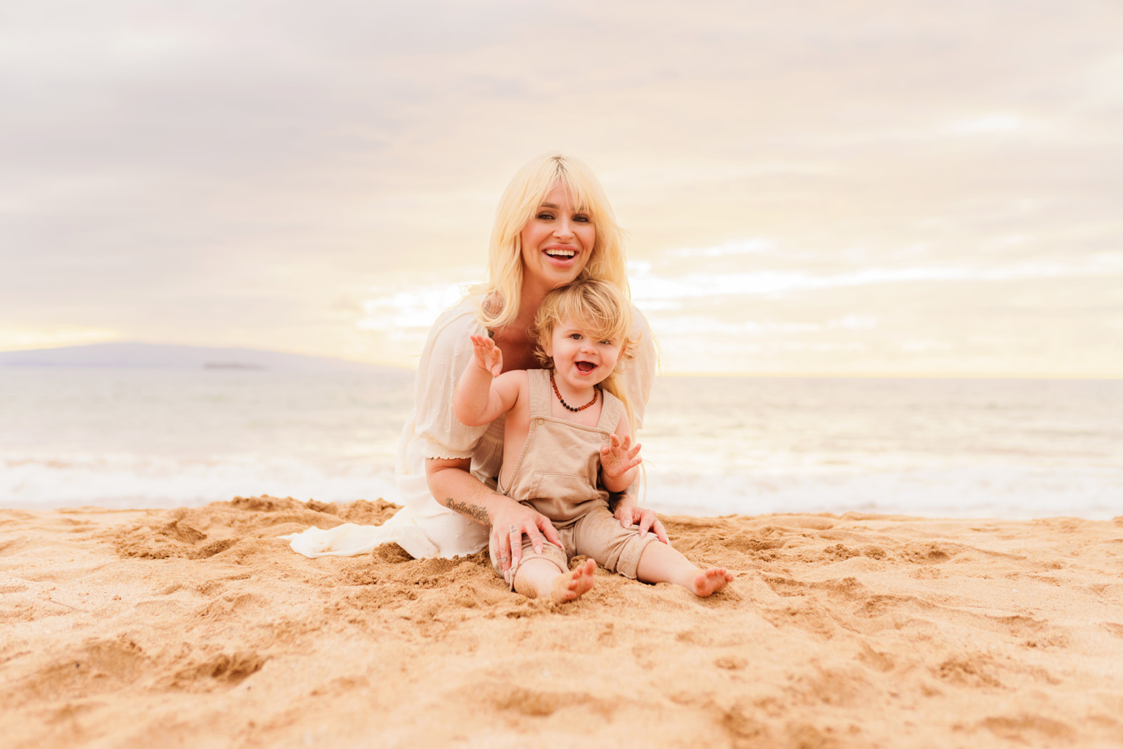 A mother and her toddler play in the sand together for a family photoshoot on the beach. 