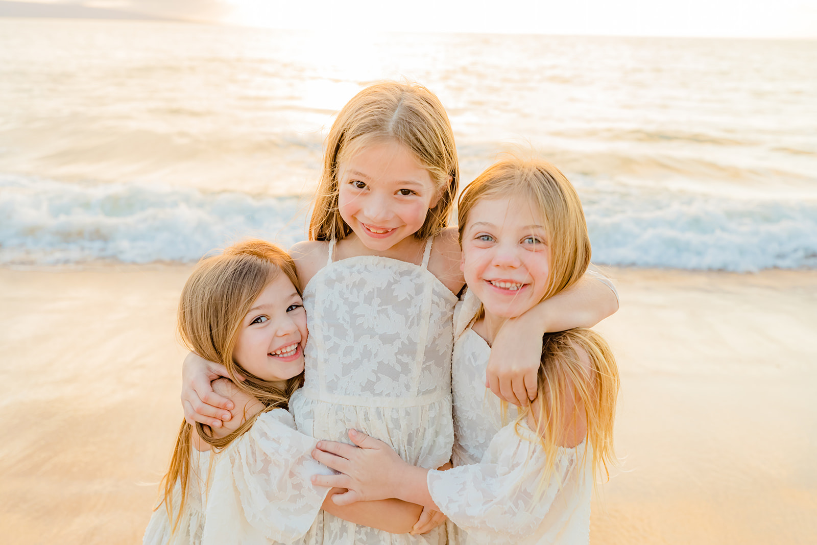 three daughters hugging on the beach in maui hawaii during a mother daughter photoshoot