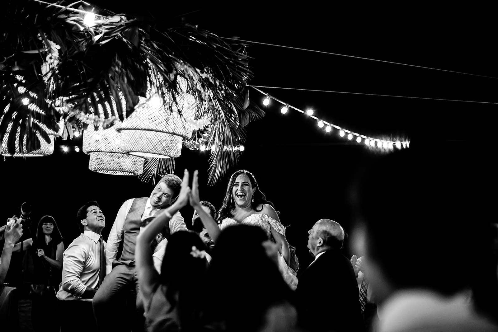 Wedding guests carry a just-married bride and groom into the reception on chairs at a fun wedding reception on Maui. 