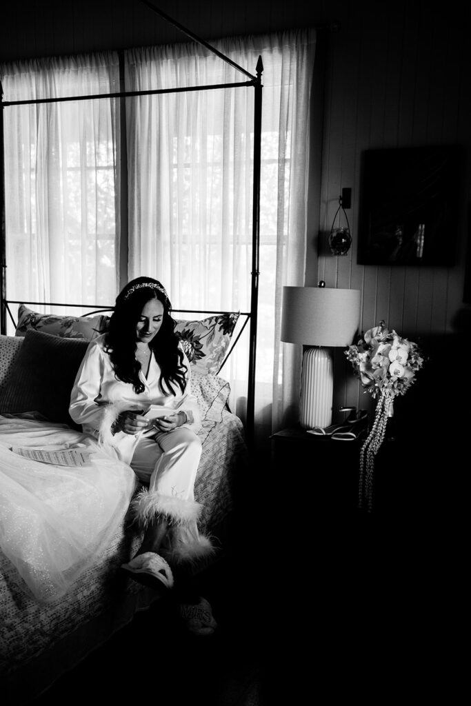 A bride reads a letter from her husband-to-be while sitting on a bed and getting ready for her wedding at Olowalu Plantation House on maui while love + water photography captures the moment.