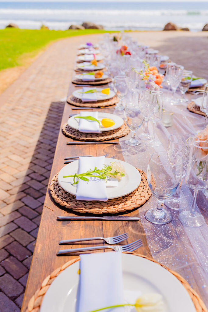 Beautiful, tropical-themed table setting for a wedding on maui by the beach at Olowalu Plantation House featuring fresh flowers and clear glassware.