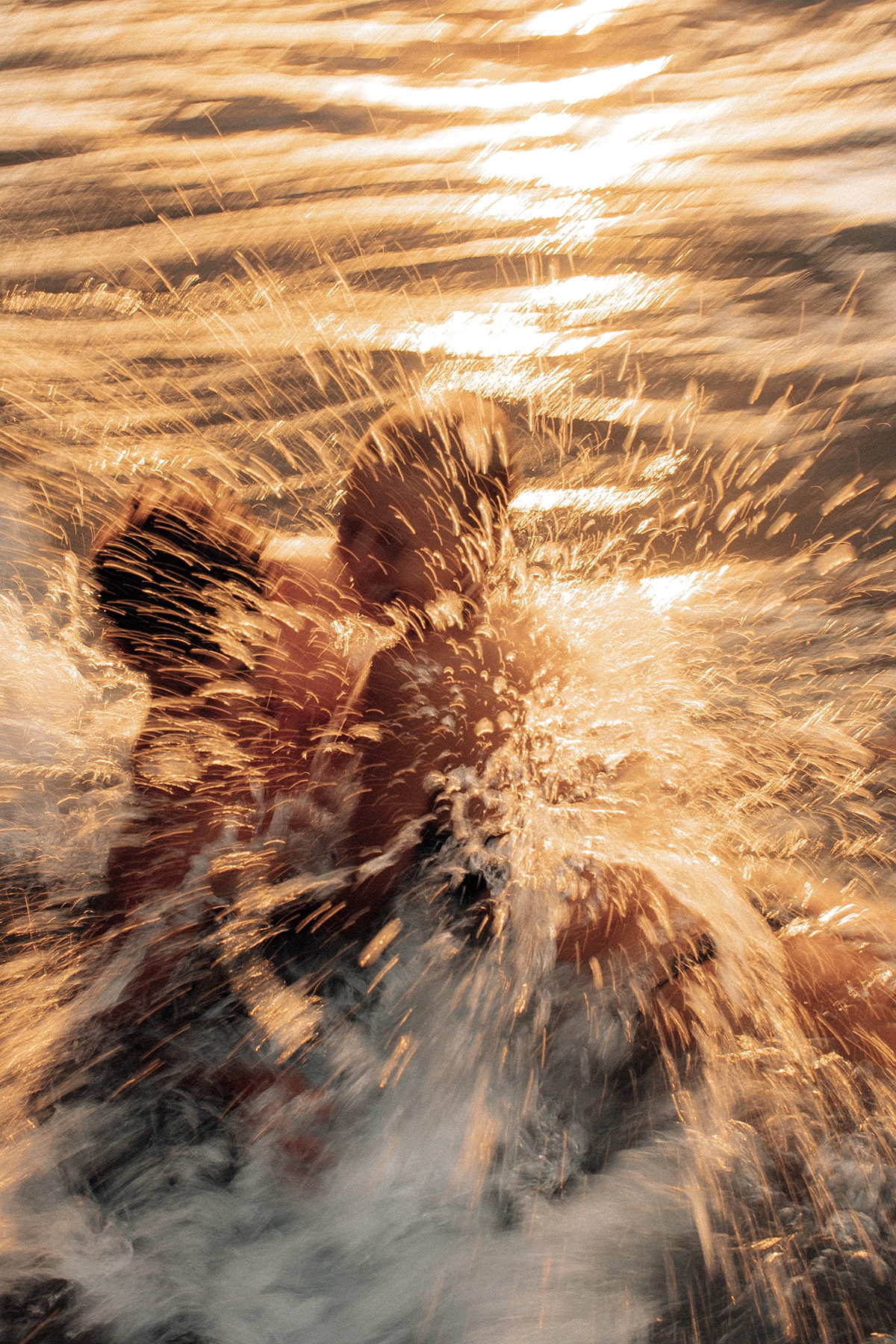 In a golden Maui sunset, a couple enjoys a romantic moment rolling in the surf, their laughter and love reflecting the beauty of the scene. Photographed by Love and Water Photography.