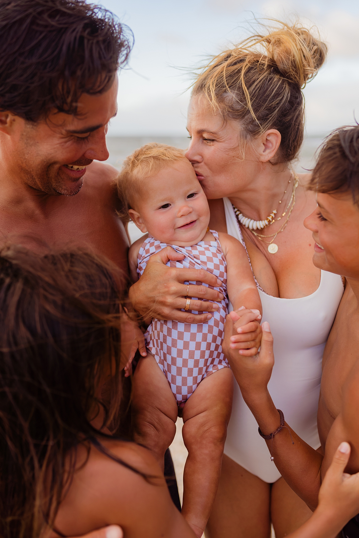 Sunset family beach photo with a mom, dad, and three children, joyfully embracing as the sun sets.