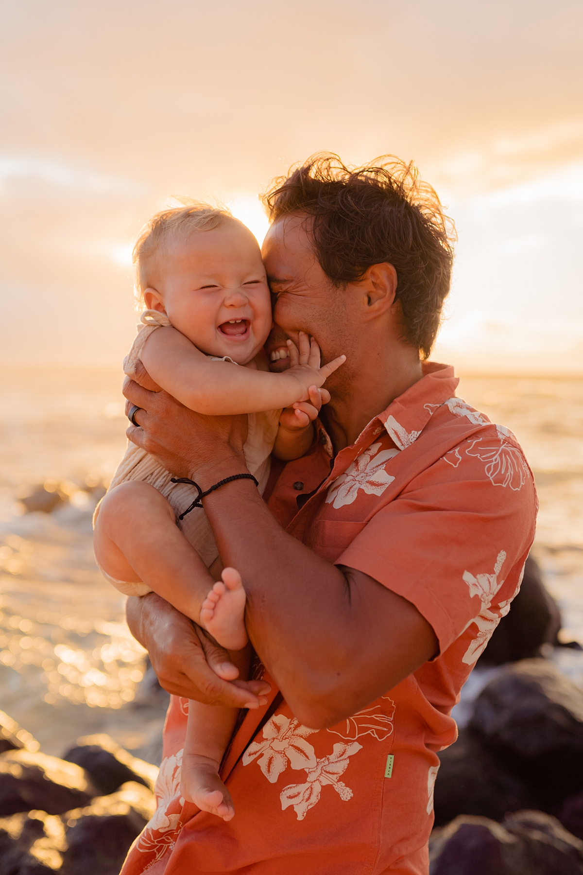 Dad holding toddler daughter who is giggling as he cuddles her close during a maui family photography session in Paia.