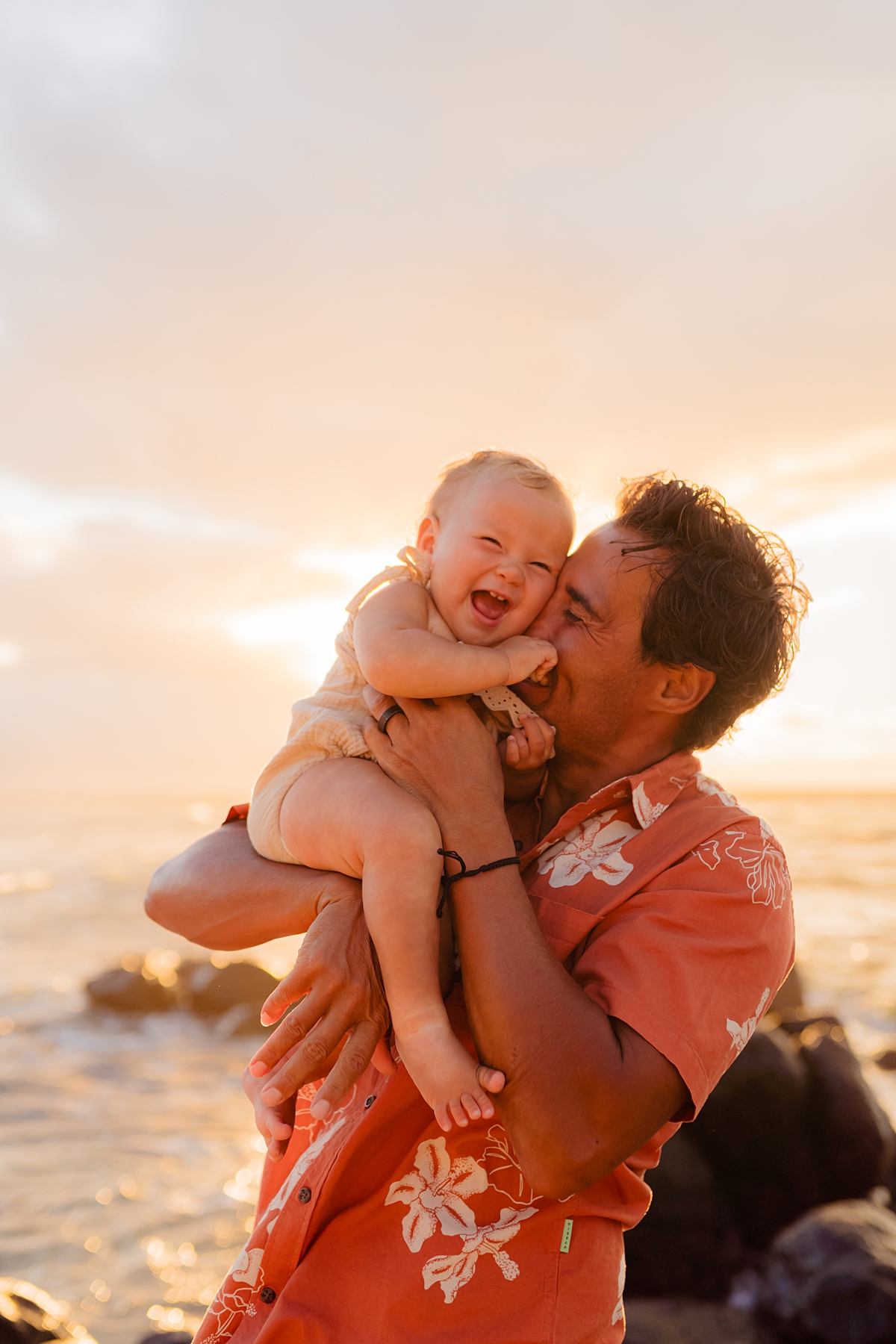 Sunset family session on a sandy beach in Maui, featuring a dad holding his daughter close, with waves gently rolling in the background.