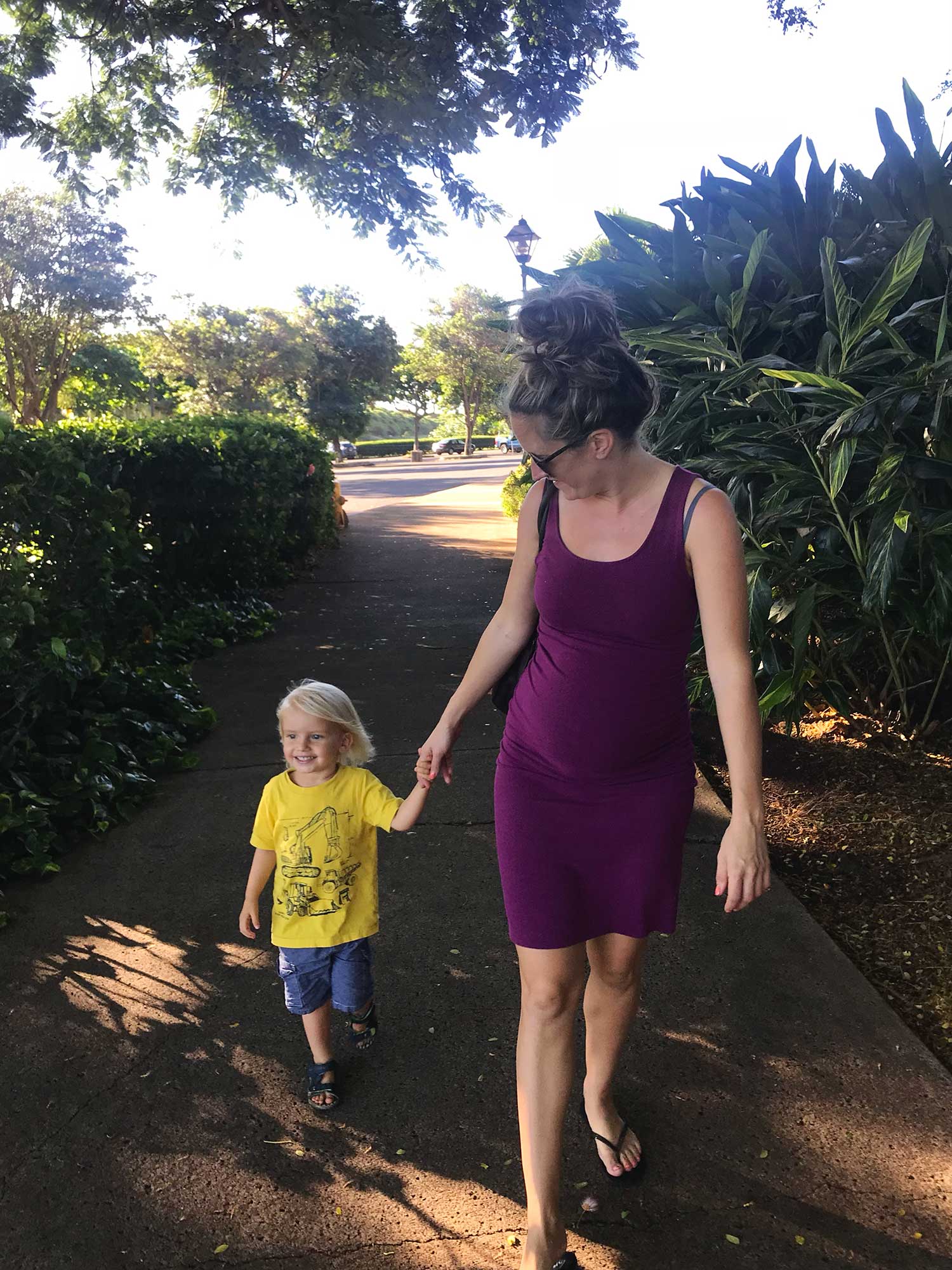 Pregnant woman holds the hand of her toddler son while walking around the Maui Tropical Plantation in Waikapu, Maui