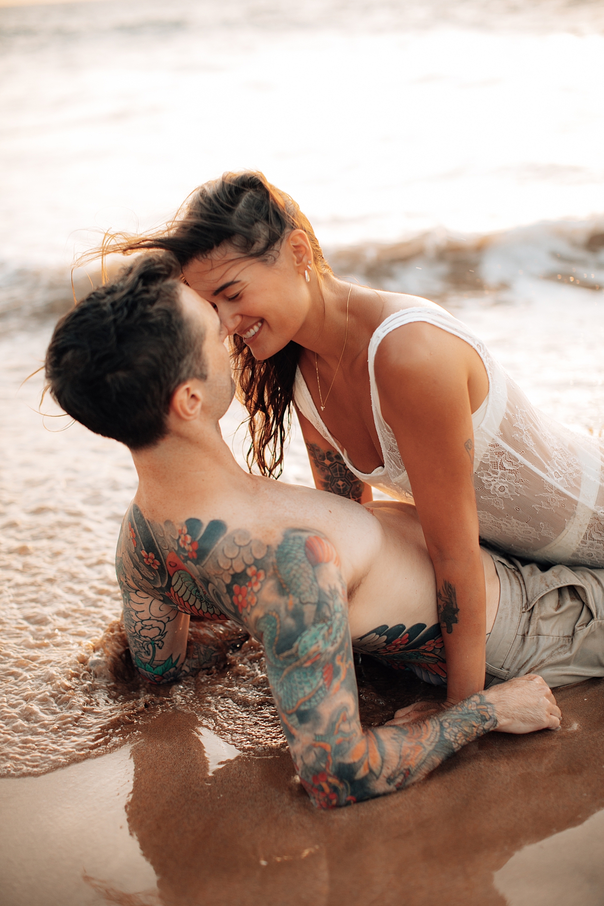 Soft light captures a couple sharing a playful moment on the sand, waves glistening in the distance at Wailea Beach.