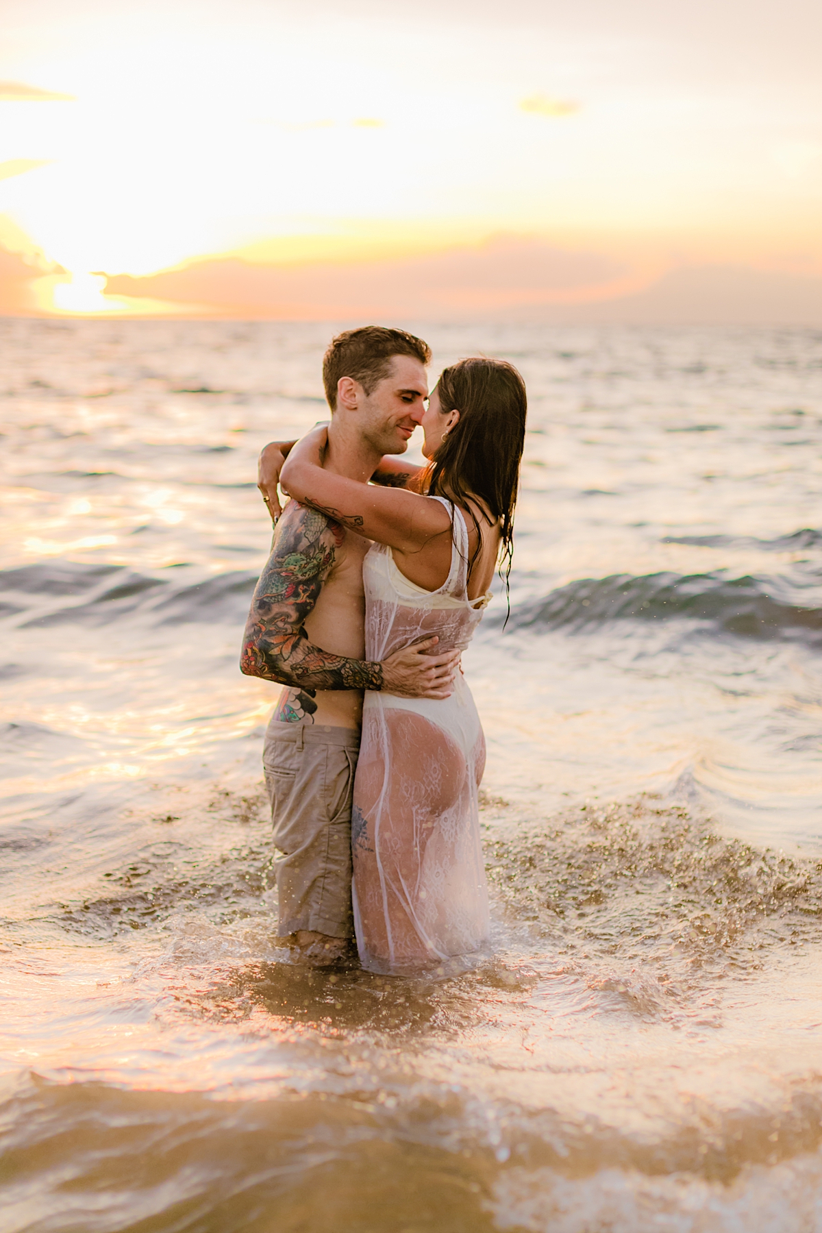 Waves gently lap at the feet of a couple embracing in the water during a sunset beach session in Wailea, Maui.