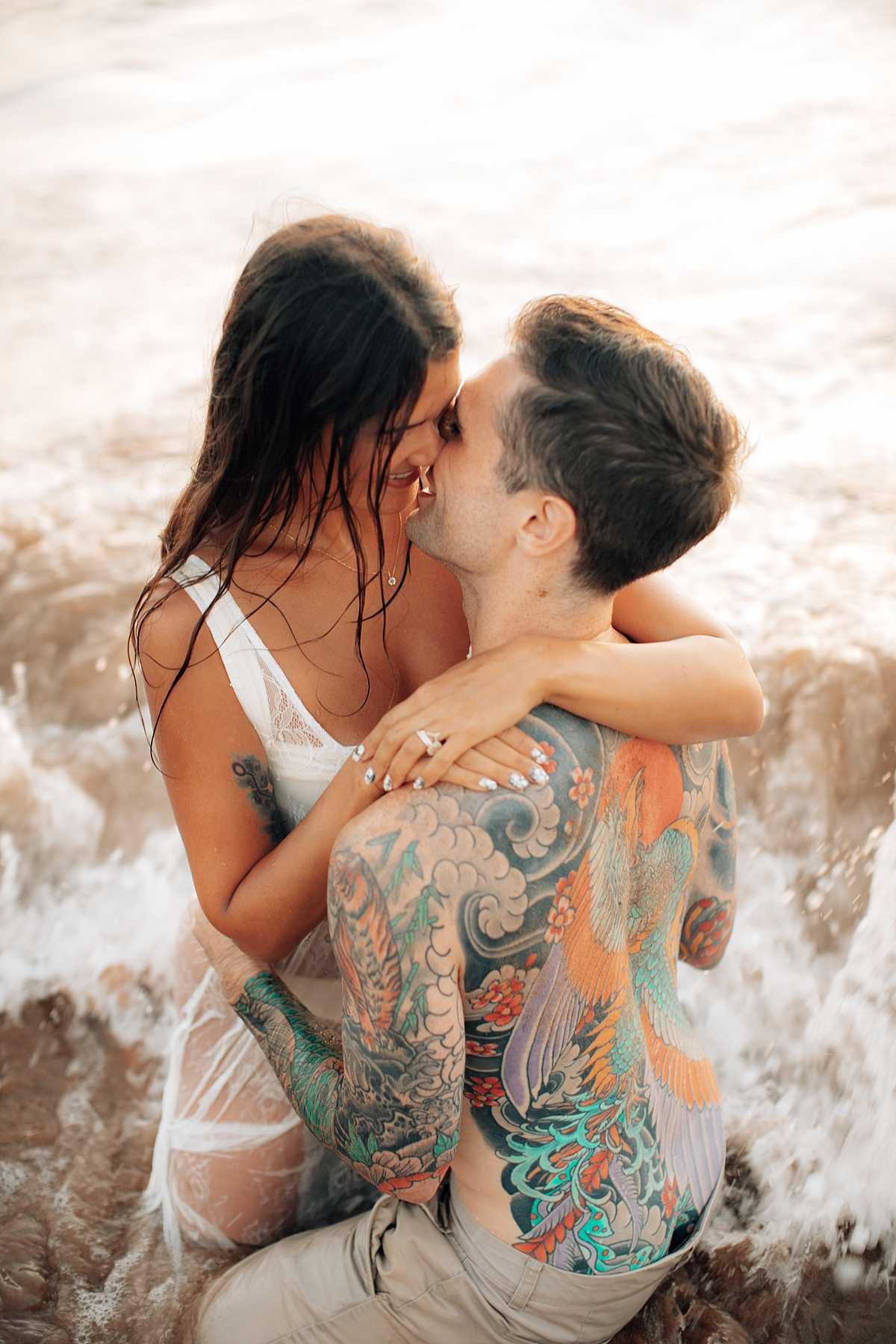 A man kisses his partner’s forehead as they lie on the sand in an intimate moment captured at a Maui beach.