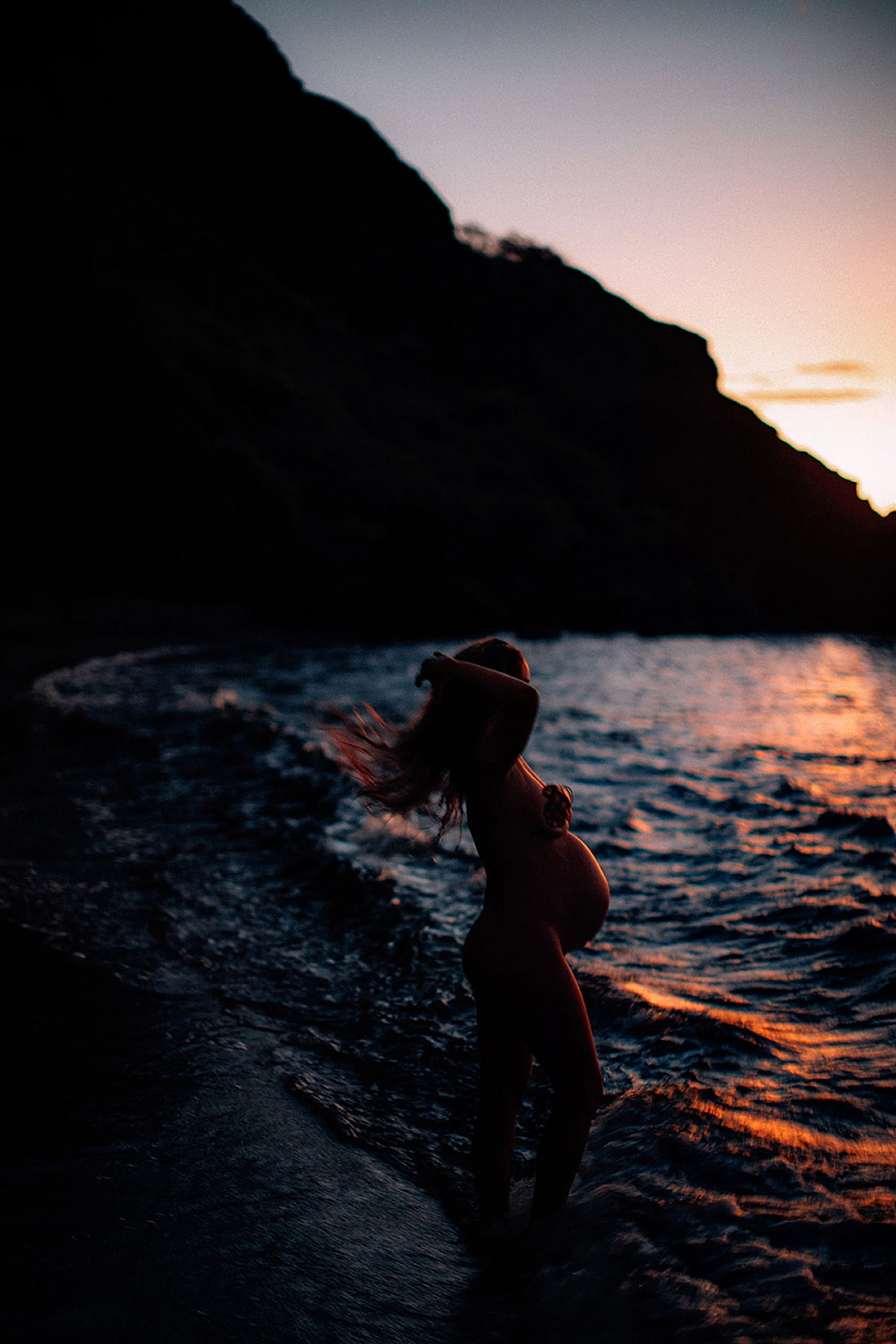 Woman tosses her hair as the last bit of sun sinks below the horizon during blue hour photoshoot in Wailea