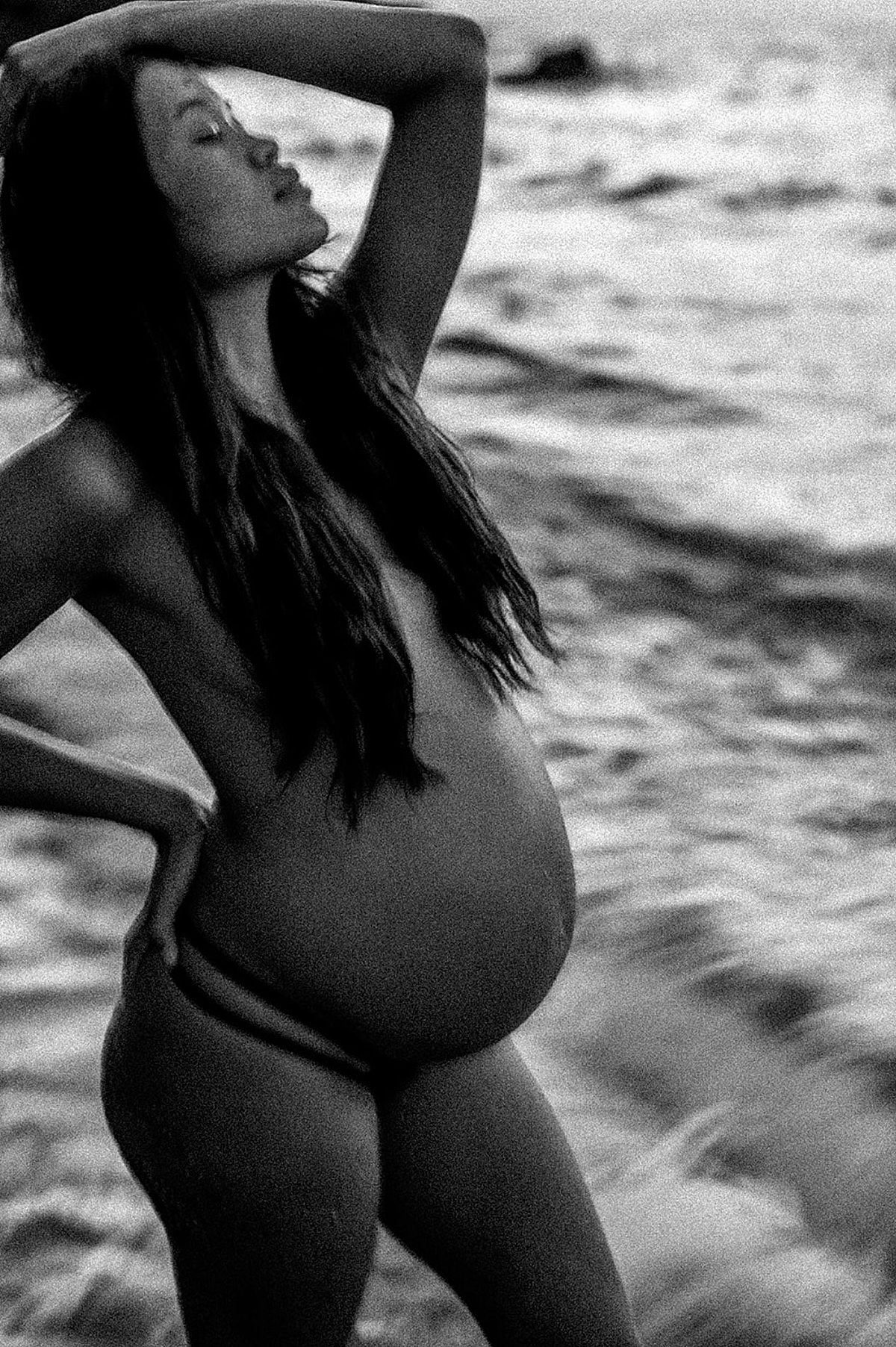 Elegant grainy maternity portrait in black and white, woman has long black hair and looks up with her eyes closed during love and water maternity session