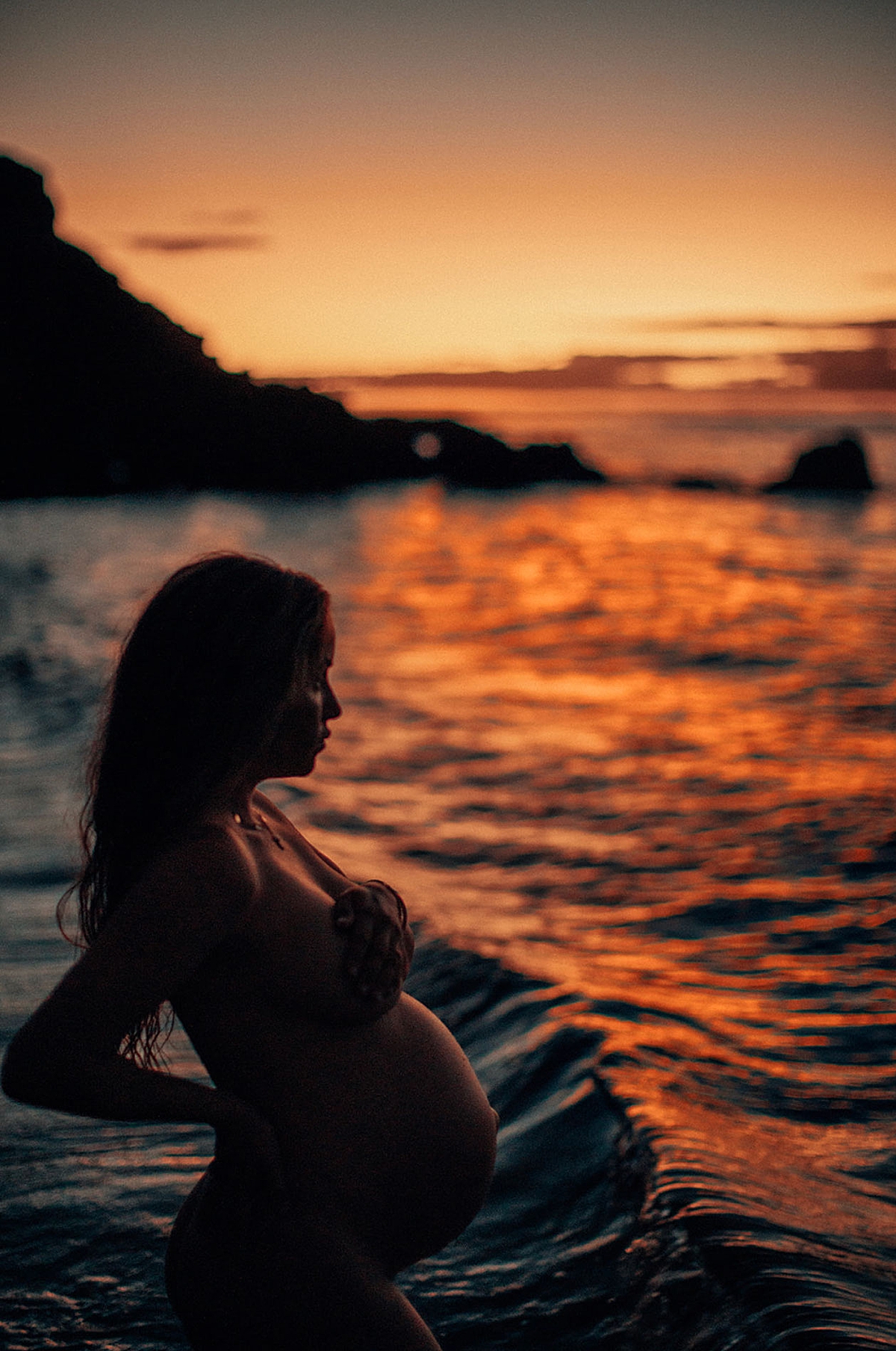 golden light wraps around an expecting mother at blue hour in hawaii