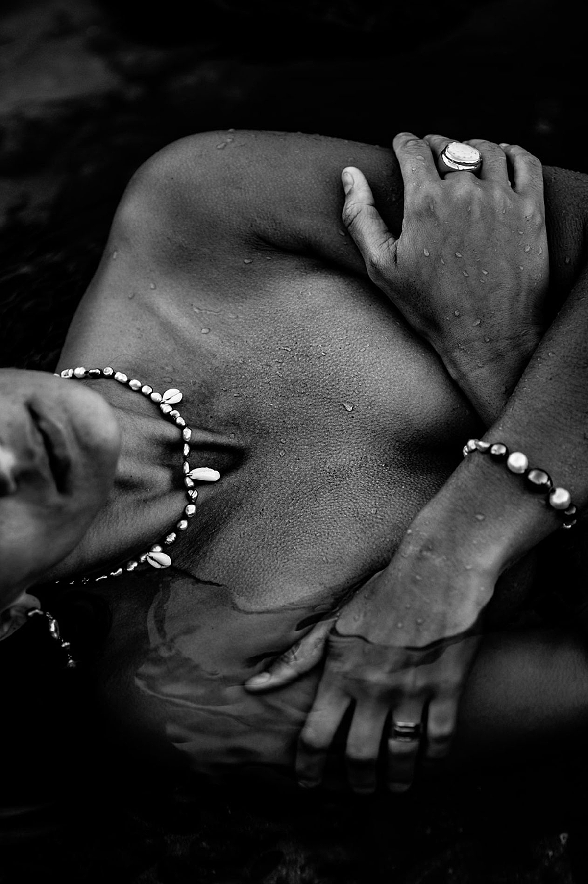 black and white boudoir portrait of woman clasping chest wearing puka perri jewelry with goosebumps in a Maui rock pool