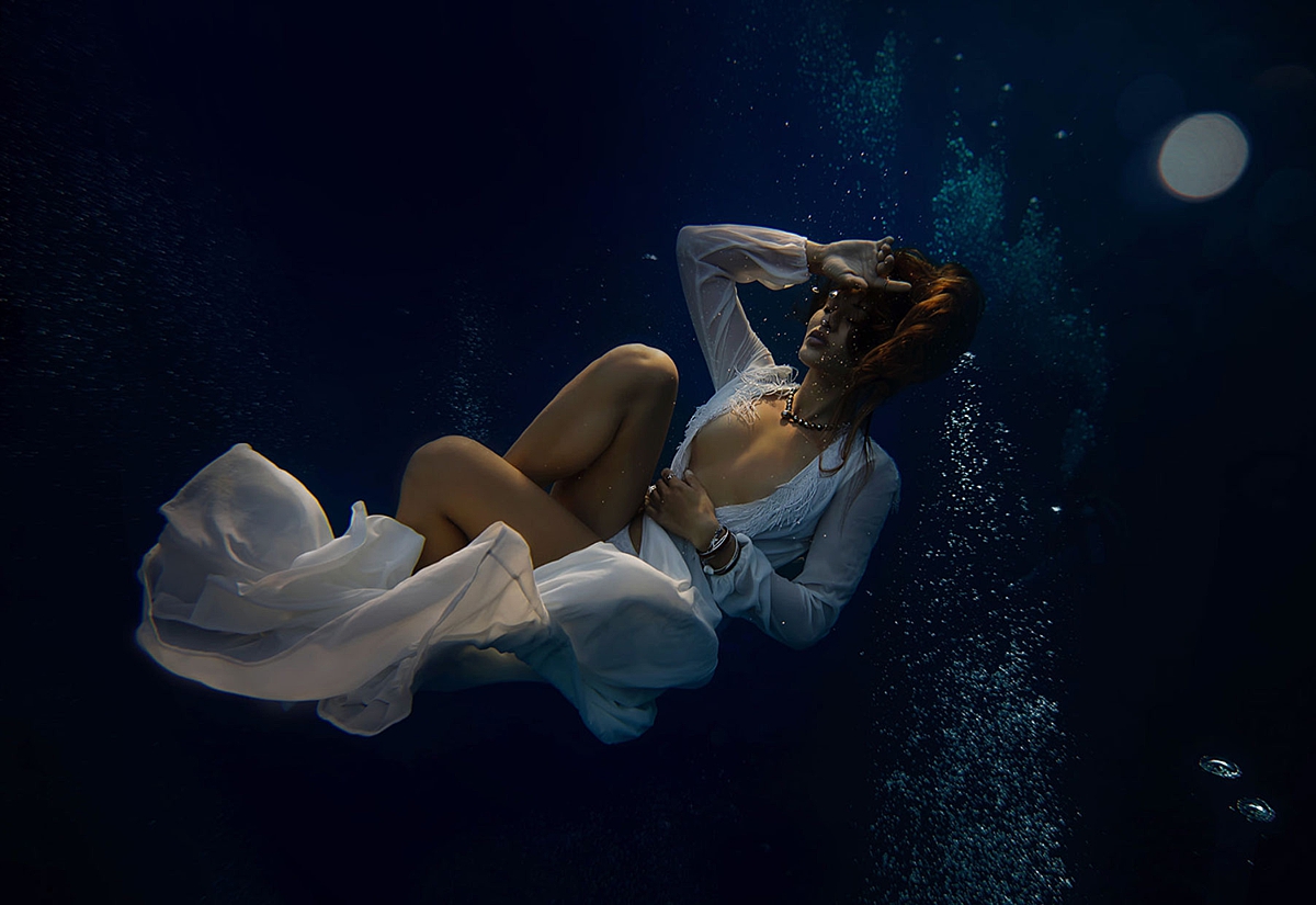 empowering underwater portrait by love and water photography featuring woman in the ocean wearing a white gown and closing her eyes