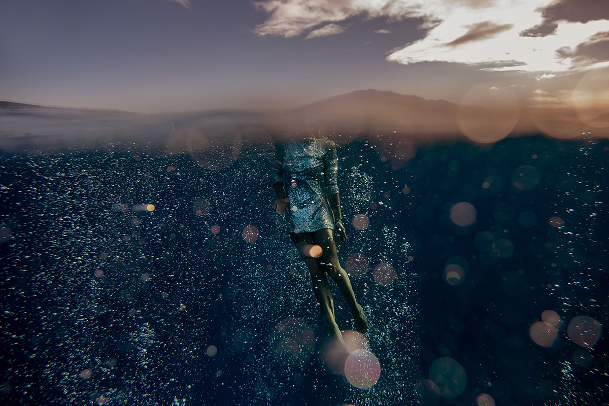 underwater image of woman in sparkly silver gown with west maui mountains in the background