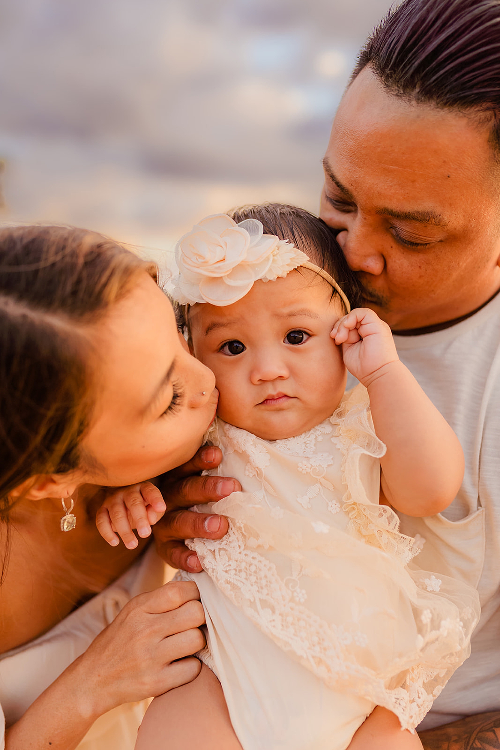 Mother and dad kiss their baby daughter's cheeks 