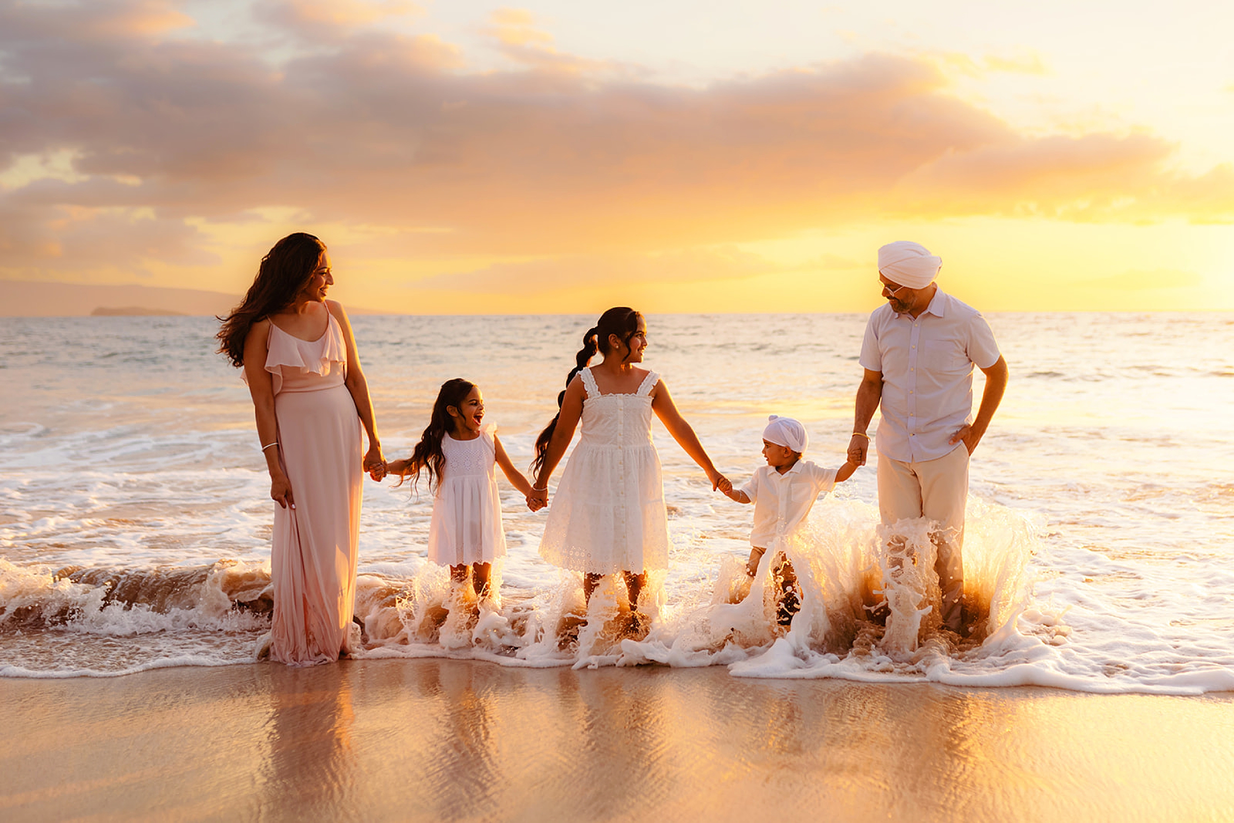 Close-up of parents holding their kids hands while getting splashed by waves on Wailea Beach, reflecting the warmth and family-friendly appeal of Maui vacations