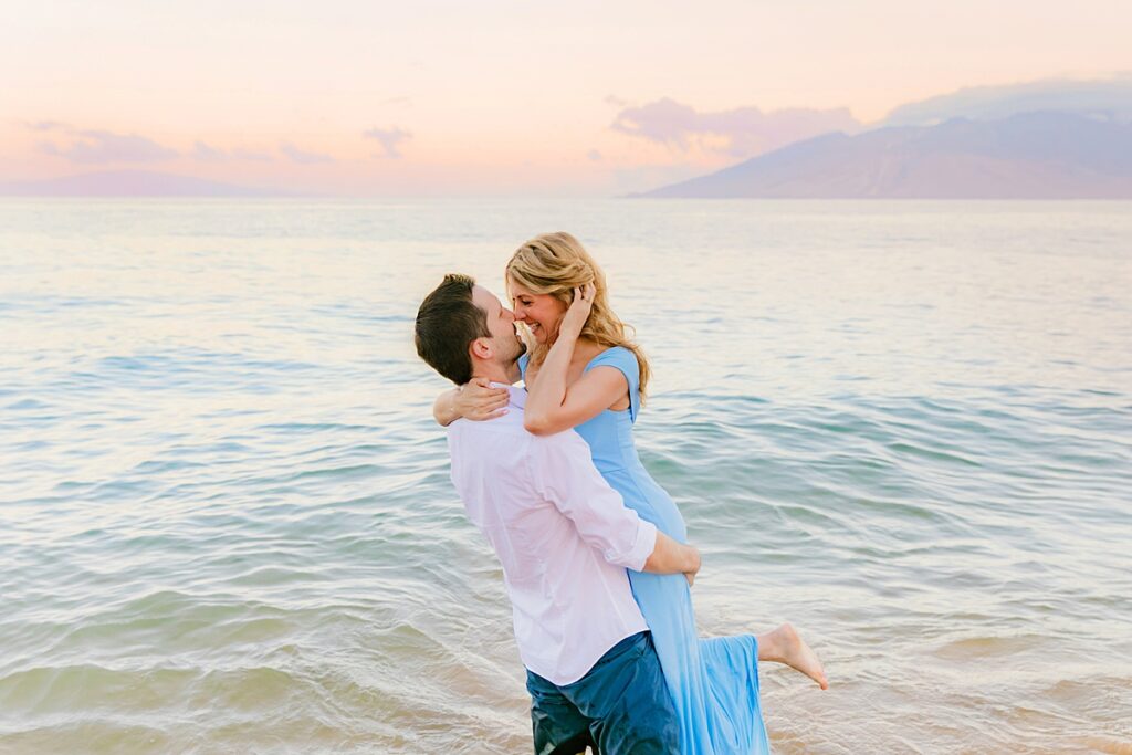 woman in blue dress jumps into her lovers arms in the ocean on a beach in Maui during their engagement portraits