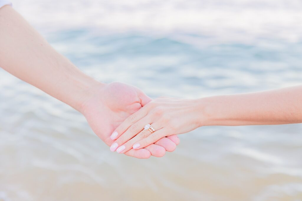 close up photo of wedding ring on bride's hand with the ocean in the backdrop