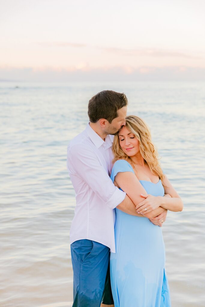 woman closes her eyes as her husband kisses her forehead in the ocean on their hawaii vacation