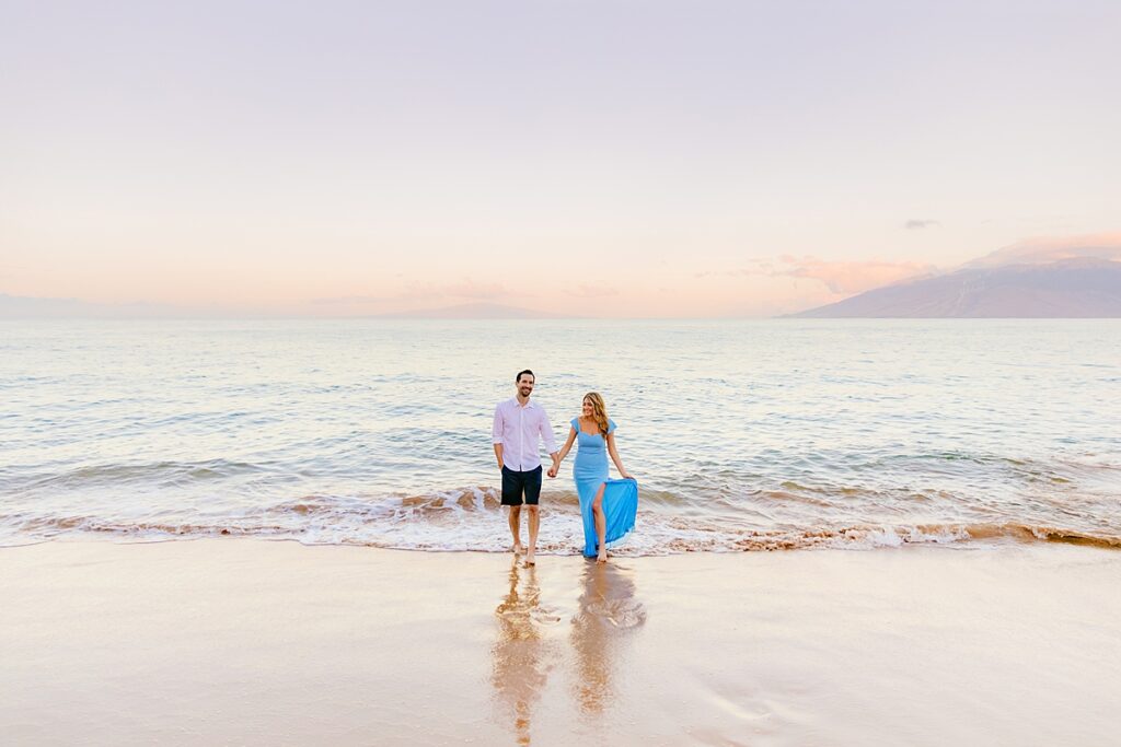 woman's dress flies in the wind as she walks on the beach on maui with her new husband